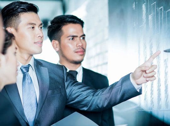 Two men in suits are looking at a wall.