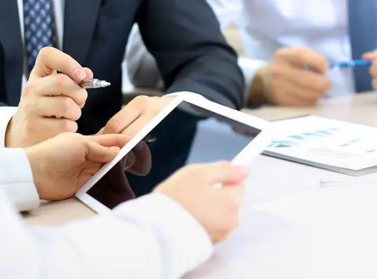 A group of people sitting at a table with two ipads.